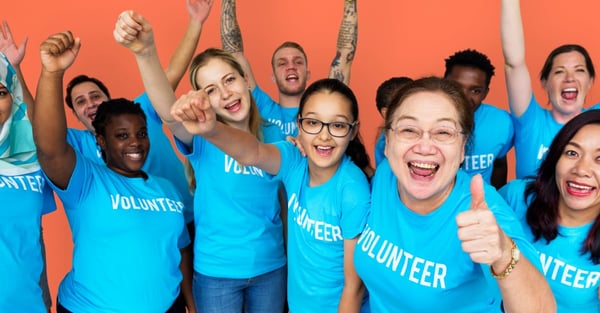 Group wearing blue volunteer T-shirts, smiling and raising their hands.