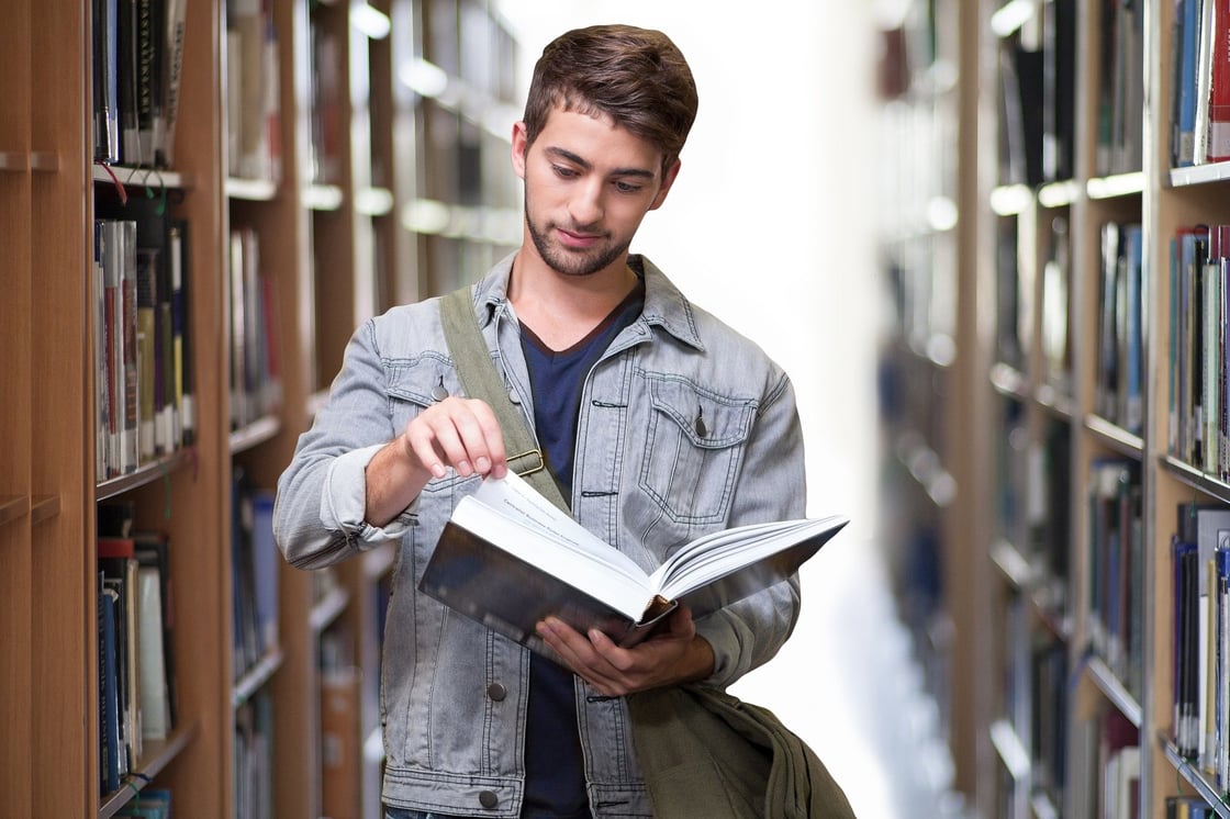 A person reading an open book between library shelves