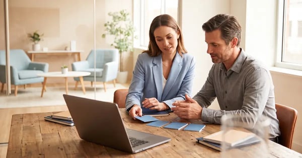 Illustrative scene of two people arranging blue cards beside a laptop at a table.