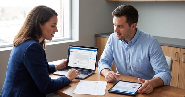 Two people review a website page layout on a laptop and tablet at an office table.