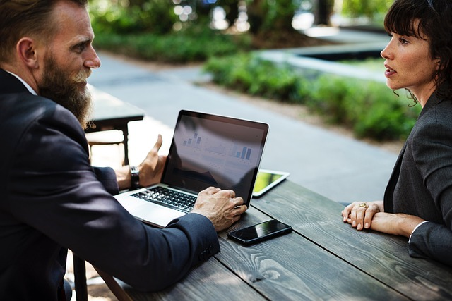 Two people reviewing charts on a laptop at an outdoor table.