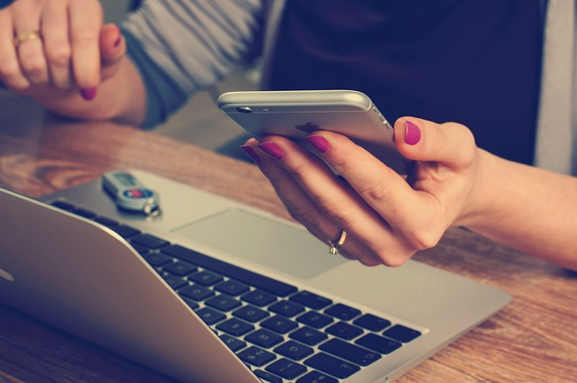 Person holding a smartphone beside an open laptop.