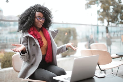 Person seated at a laptop and gesturing with both hands